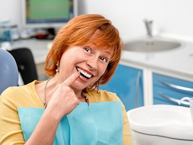 Woman in dental chair pointing to her dentures and smiling